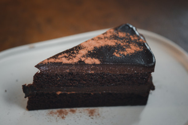 在白色的盘子上用巧克力粉装饰的美味的黑巧克力软糖蛋糕三角片图片下载