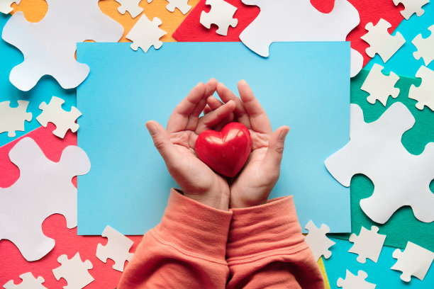 4月2日世界关爱自闭症日的创意设计。俯视图，手捧红石心图片下载