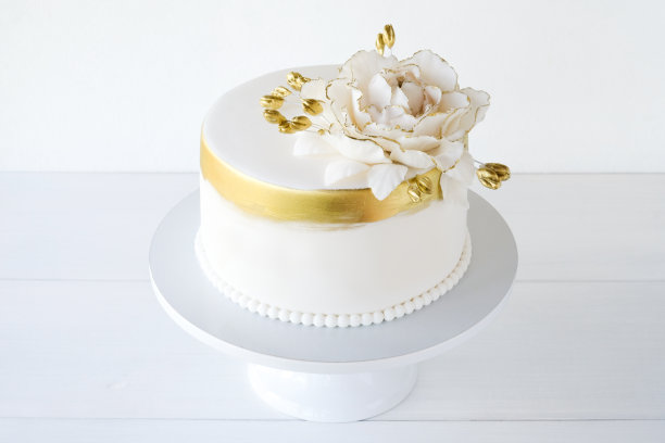 白色的婚礼蛋糕，白色的背景上装饰着金色的花朵。图片下载