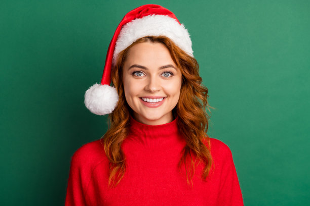 照片正面漂亮的女士看摄像头微笑穿红色套衫圣诞头饰孤立的绿色背景图片下载