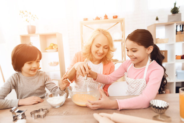 快乐的小女孩在牛奶碗里打鸡蛋，她的弟弟在倒面粉。图片下载