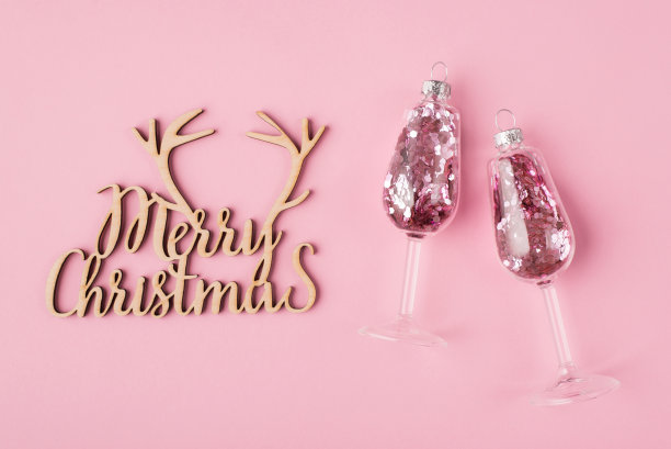 圣诞节的概念。上面俯瞰照片的葡萄酒杯与粉红色的纸屑内和木制手工圣诞标志孤立在柔和的粉红色背景图片下载