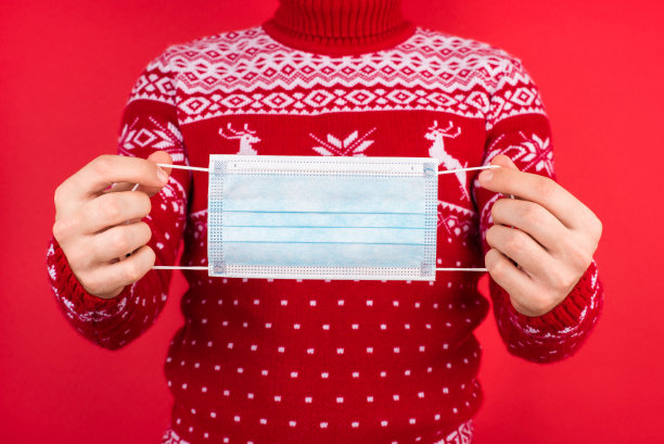 圣诞节与冠状病毒检疫的概念。近距离照片的男人在红色的冬季毛衣与鹿持有外科口罩隔离在红色的背景图片下载