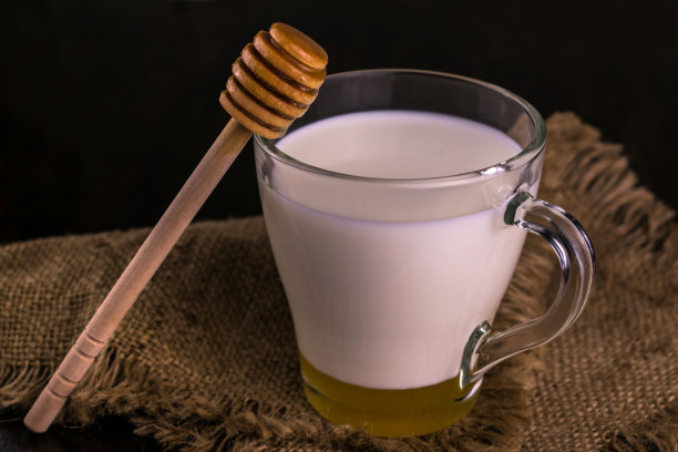 牛奶和蜂蜜在一个杯子在黑暗的背景。特写镜头。图片下载