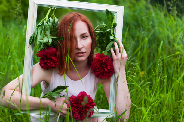 一个红发白人妇女，手里拿着一个画着红花的画框。婚礼photozone概念。图片下载
