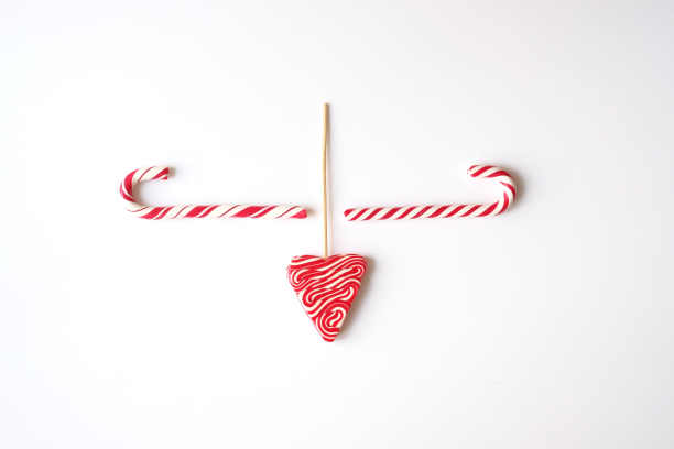平的。新年和圣诞主题。三个红白相间的棒棒糖看起来像牛头。位于中心。白色背景。图片下载