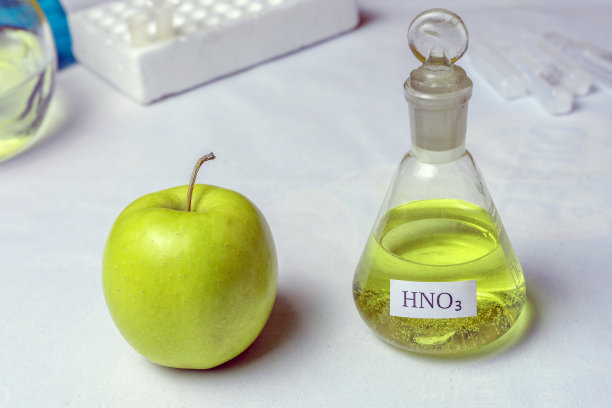 一个苹果和一个标有硝酸-硝酸的化学瓶。硝酸盐和转基因生物存在的概念图片下载