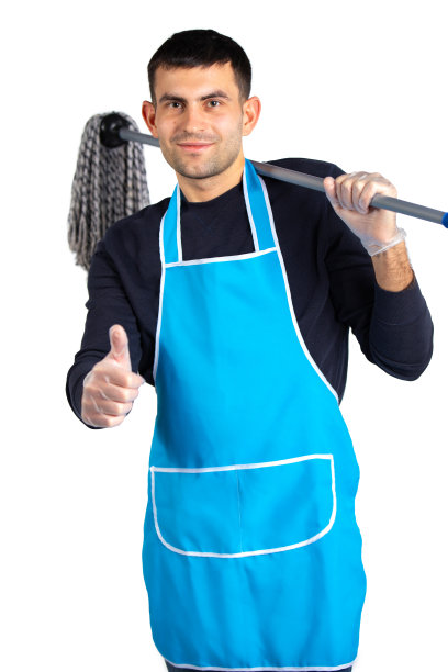 一个穿着围裙、戴着手套、肩上扛着拖把的男人摆好姿势，向镜头展示他的班级。性别包容性。照片上的白色背景与空白的边空间。图片下载