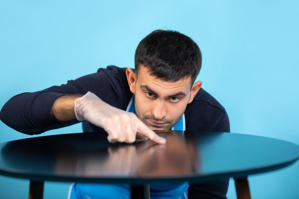 一个戴橡胶手套的男人检查桌子的清洁程度。蓝色背景上的照片。性别刻板印象。图片下载