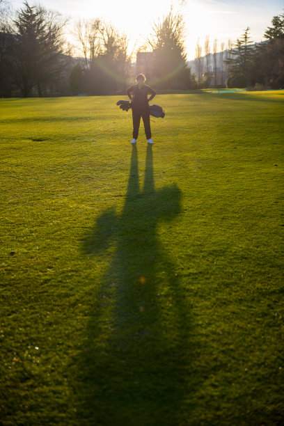 高尔夫球手与她的高尔夫球袋站在日光和阴影的球道图片下载