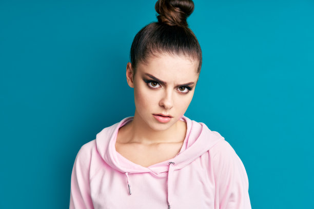 年轻严肃的愤怒的女人在蓝色背景上接近肖像图片下载