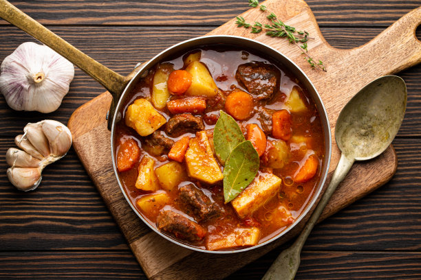 美味的炖肉，土豆，胡萝卜和肉汁在古老的乡村铜锅上，棕色的木制背景从上面。传统的冬季和秋季菜肴炖牛肉和蔬菜图片下载