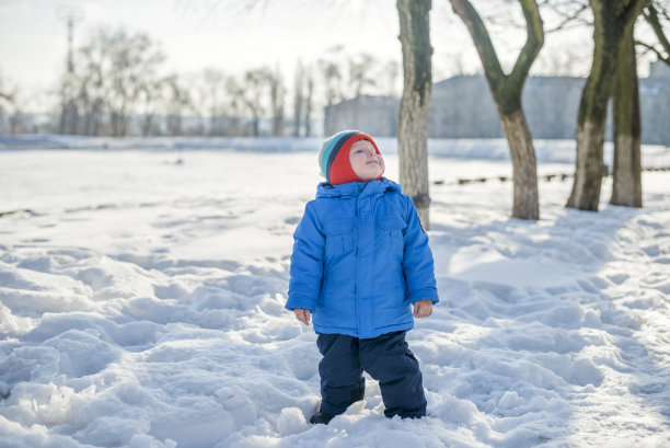 冬天，小孩子走在下雪的街道上。冬天穿得暖和的孩子走在街上图片下载