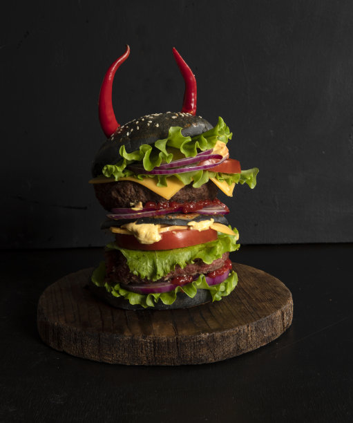 巨大的黑色汉堡，多汁的牛肉馅饼，西红柿，奶酪和酱汁，用红辣椒装饰图片下载