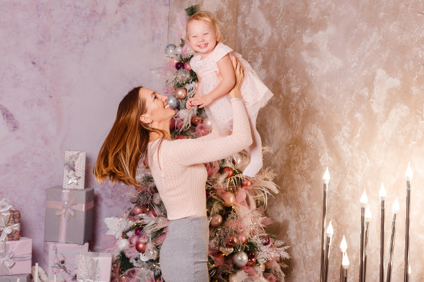 圣诞节快乐的年轻妇女和穿着粉红色衣服的女婴。在圣诞节摄影棚里为母女拍摄粉红色的照片图片下载