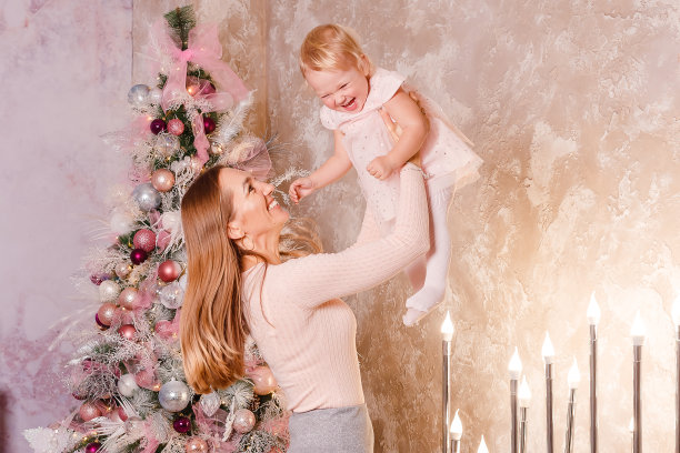 圣诞节快乐的年轻妇女和穿着粉红色衣服的女婴。在圣诞节摄影棚里为母女拍摄粉红色的照片图片下载