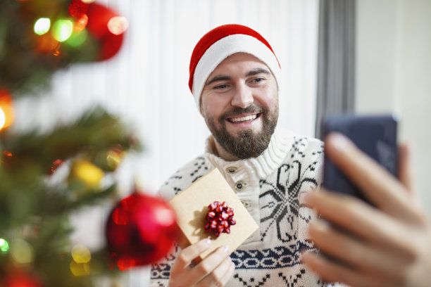 年轻人打电话与圣诞树和礼物包是分享礼物。图片下载