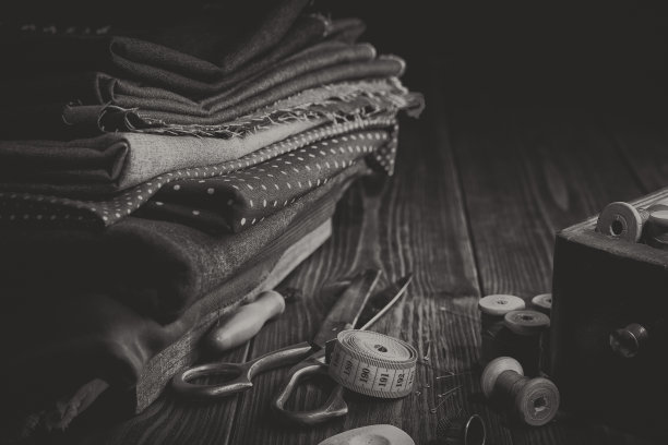 缝纫用织物堆，剪刀，卷尺，线轴，装缝纫配件的木箱。黑白风格照片。图片下载