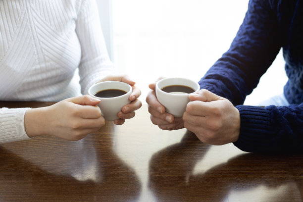 女人和男人的手拿着咖啡杯放在木桌的背景上图片下载