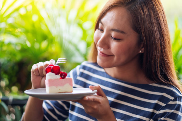 一位年轻美丽的亚洲女子拿着一块草莓芝士蛋糕吃着图片下载