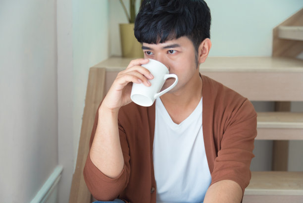 穿着针织外套的英俊男人喝着咖啡，望着窗外。享受工作日的休闲概念图片下载