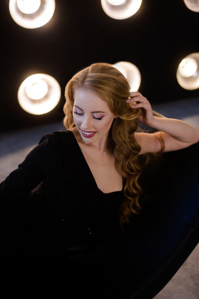 一个美丽时尚的年轻女子穿着优雅的裙子性感地躺在沙发上，背景是明亮的led灯。欢乐的金发女孩在派对上休息。预约心理治疗师图片下载