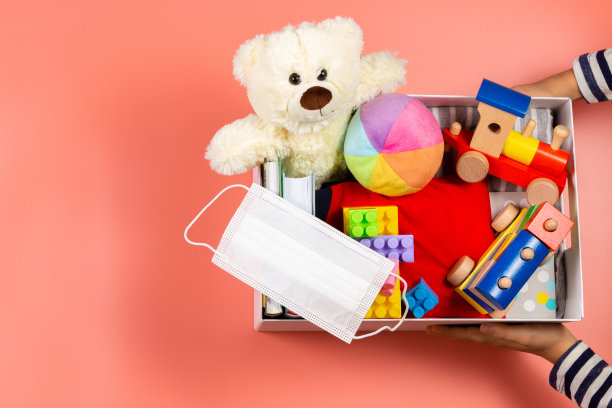 捐赠的概念。孩子的手与捐赠箱，衣服，书籍和玩具在粉红色的背景。俯视图图片下载