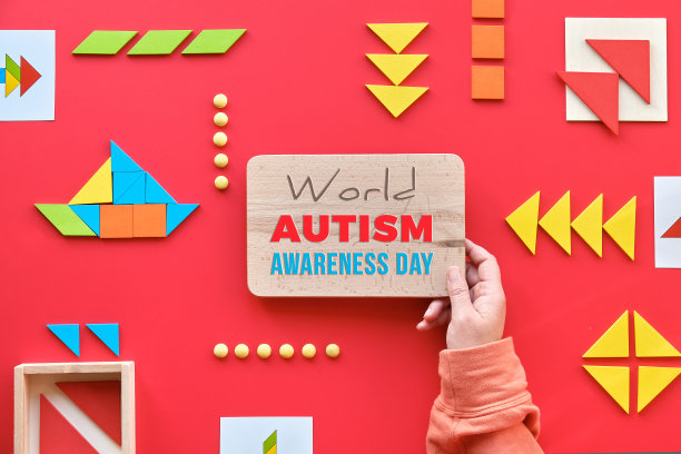 这是世界自闭症日的创意设计，手拿文字。七巧板拼图，平躺在红色上图片下载