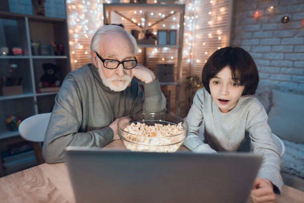 爷爷和孙子晚上在家看电影吃爆米花。图片下载