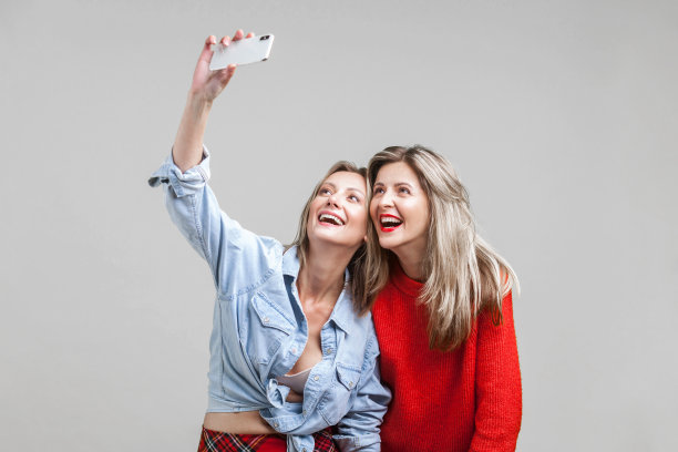 女性朋友享受时光。肖像的两个美女在时尚的衣服自拍，孤立的灰色背景图片下载