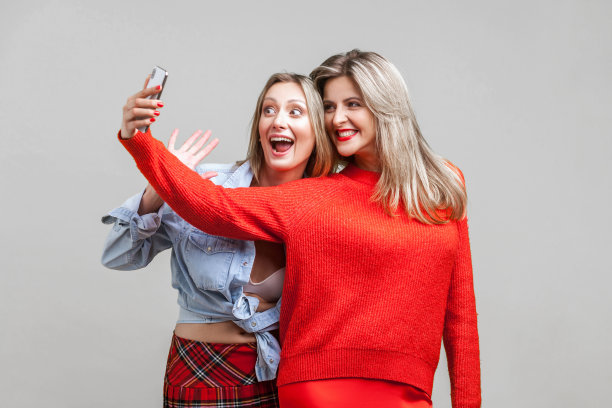 最好的朋友在玩。穿着时髦的衣服自拍的快乐女人的肖像，孤立在灰色的背景图片下载