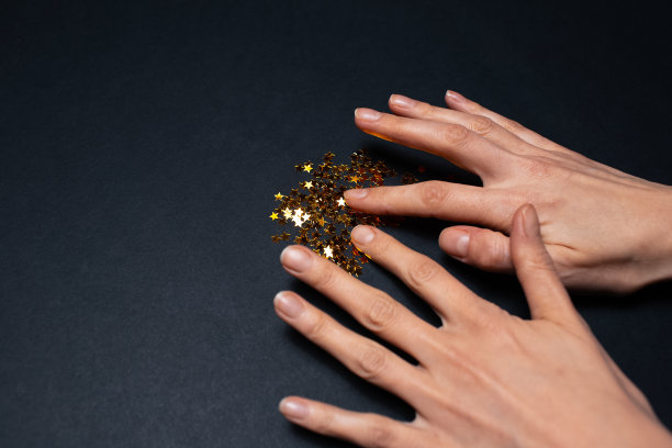 手的特写准备装饰金色的星星在黑色的背景。图片下载