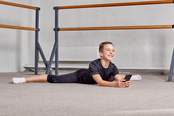 一个年轻人在做劈叉，手里拿着手机微笑着。图片下载