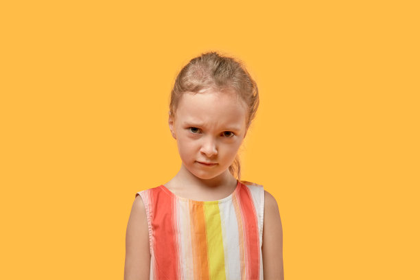 伤心可爱的女孩低着头看着镜头。橙色背景。图片下载