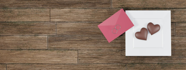 两颗心形巧克力放在白色方形盘子上，上面有红包和两枚订婚戒指图片下载