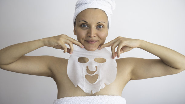 一个年轻女子裹着一条白毛巾，戴着化妆面具。脸上脱皮面具。Spa美容。图片下载