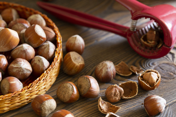 榛子和一个红色的胡桃夹子在一个柳条篮子在木板上，坚果壳，深色照片。图片下载