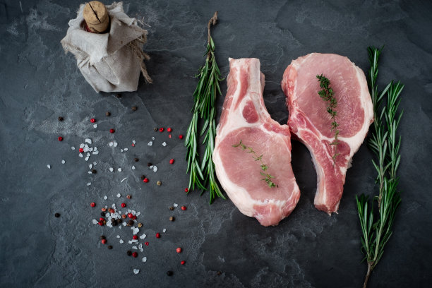 带骨的生猪肉，配上调味料的烤里脊，放在石凳上。图片下载