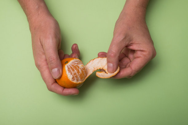 人的手剥一个有机橘子在绿色的背景图片下载