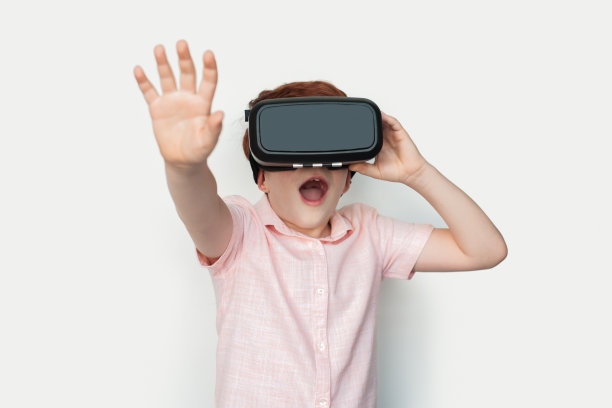 小白种人姜黄色男孩戴着虚拟现实耳机正在触摸工作室白色墙壁上的东西图片下载