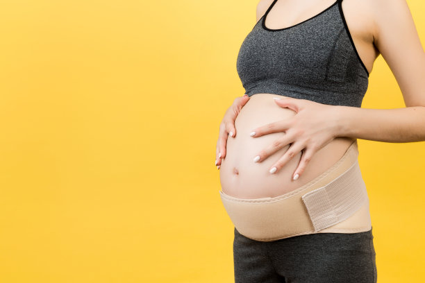 裁剪的图像孕妇穿着弹性绷带，以防止疼痛在背部黄色背景与复制空间。骨科腹部支撑带概念图片下载