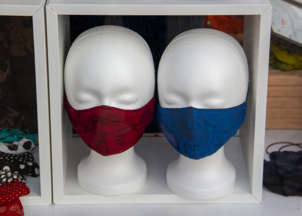 Covid-19冠状病毒的概念。两个用聚苯乙烯泡沫做的头，每个都有一个防护面具，一个有蓝色记号，另一个有红色记号。大流行病。社会距离。医疗保健。病毒。隔离。图片下载