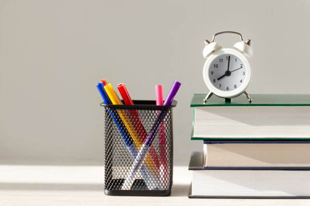 教育时代与学习的概念。闹钟在一堆书与文具。图片下载