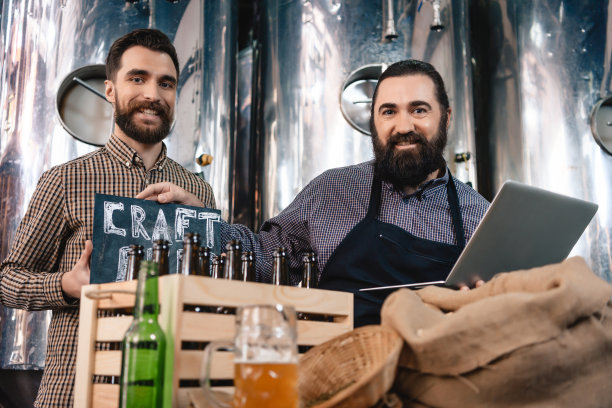 两个微笑的男人展示牌子，上面写着精酿啤酒。精酿啤酒生产。图片下载