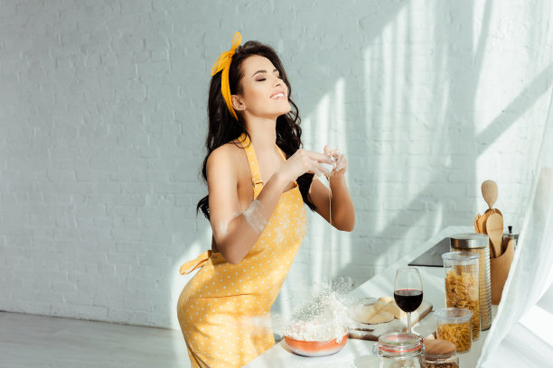 穿着围裙的微笑女孩在厨房的工作台上，一边在面粉中添加鸡蛋，一边烹饪图片下载