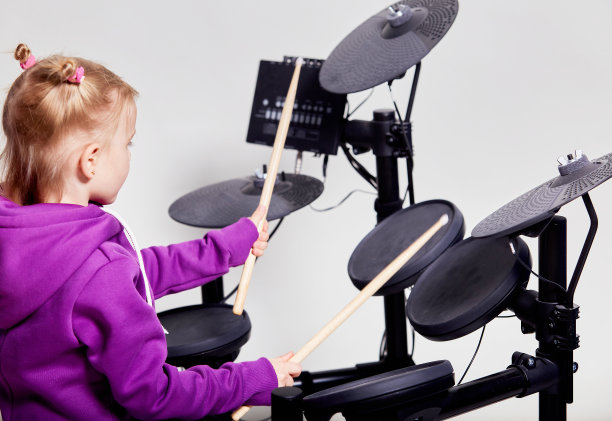 快乐的白人小女孩鼓手。在音乐学校学习打鼓或使用电子鼓的女孩。情感上的肖像。模拟，灰色背景的工作室。免费的广告空间。图片下载