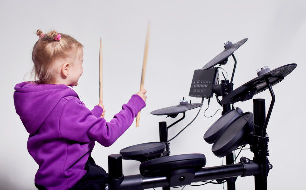 快乐的白人小女孩鼓手。在音乐学校学习打鼓或使用电子鼓的女孩。情感上的肖像。模拟，灰色背景的工作室。免费的广告空间。图片下载