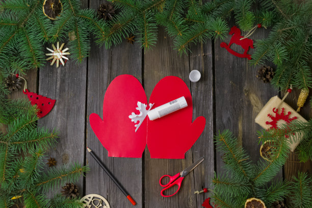 自制圣诞及新年贺卡。在一个有树枝的木桌上，红色的纸手套上有一片白色的雪花。圣诞指示。装饰品。礼物。一步一步来。平的。俯视图图片下载