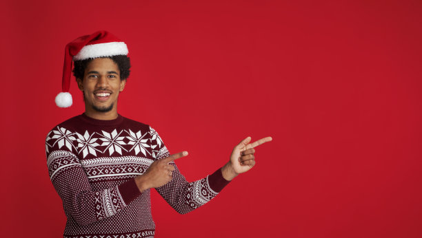 快乐的年轻非洲裔美国人在圣诞老人的帽子和图案的毛衣手指在自由的空间图片下载