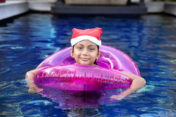 戴着圣诞老人帽子的混血男孩在游泳池里微笑。图片下载
